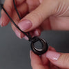 demo video of a black circle ashes urn necklace. the video shows a woman's hands unscrewing the necklace then filing it with ashes.