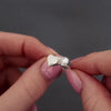 womans hands holding a silver wrap heart ring. the video shows a demonstration of filling the ring with ashes by unscrewing the screw with a screwdriver and using a funnel to scoop ashes into the ring.