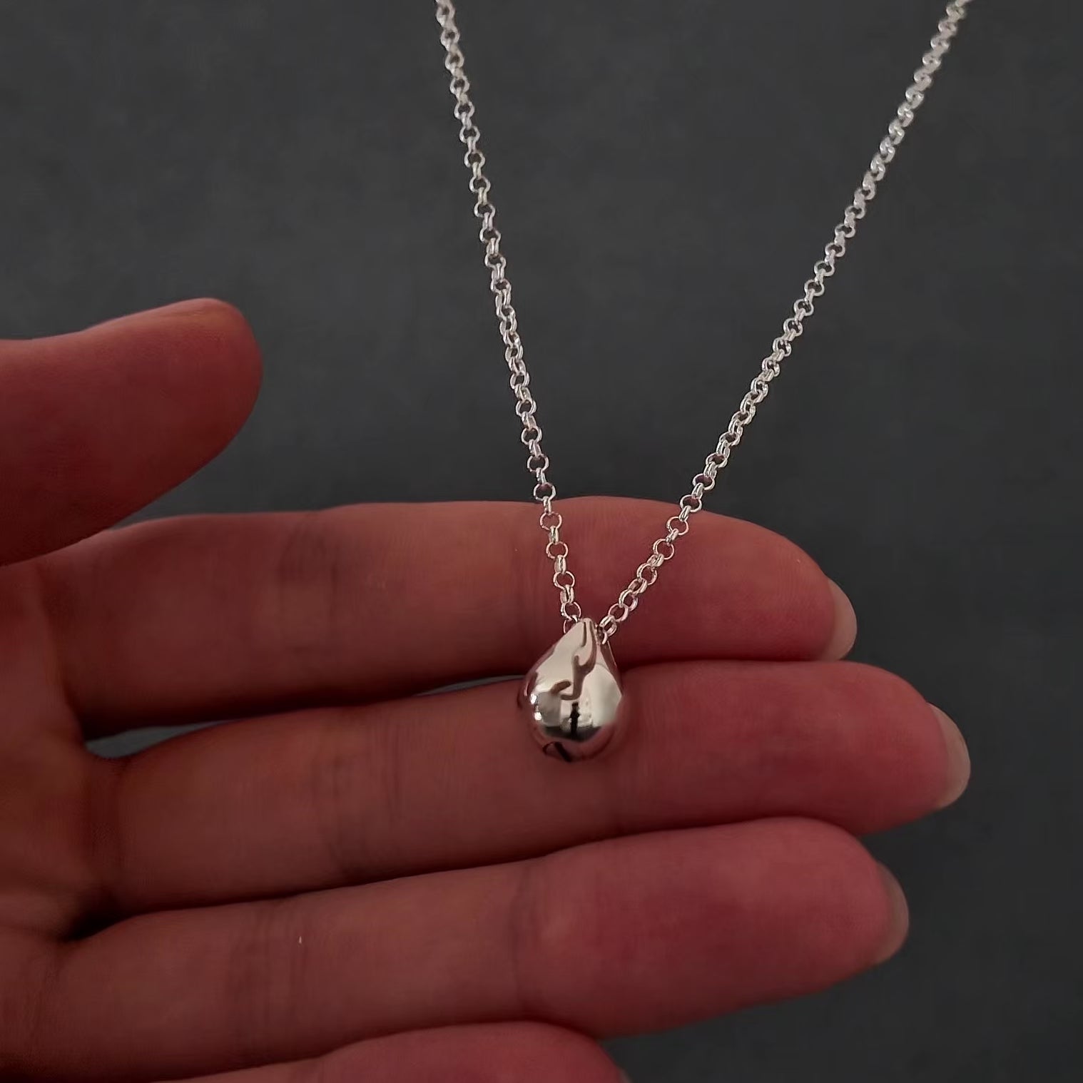 womans with pink nails hands showing a silver droplet urn necklace. she is demonstrating how to fill the necklace with cremation ashes by unscrewing the bottom with a screw driver and using a funnel to fill the pendant.