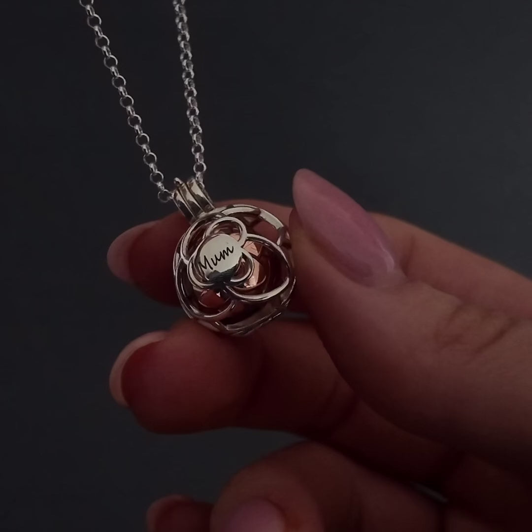 womans hands with pink nails demonstrating how to fill a rose flower ball urn agaisnt a dark background. It shows her unscrewing the screw and using a funnel to fill the urn with ashes. its then displayed in a grey jewellery box at the end.