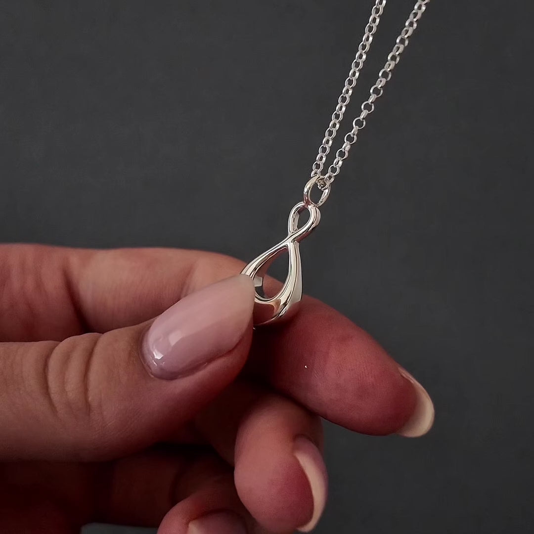 Demo video of womans hands with pink nails showing how to fill a silver infinity urn necklace pendant. it shows her unscrewing the bottom of the pendant with a screwdriver and using a funnel to fill the pendant with cremation ashes. the screw is then screwed back on and the necklace is displayed in a grey jewellery box. 