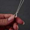 Demo video of womans hands with pink nails showing how to fill a silver infinity urn necklace pendant. it shows her unscrewing the bottom of the pendant with a screwdriver and using a funnel to fill the pendant with cremation ashes. the screw is then screwed back on and the necklace is displayed in a grey jewellery box. 