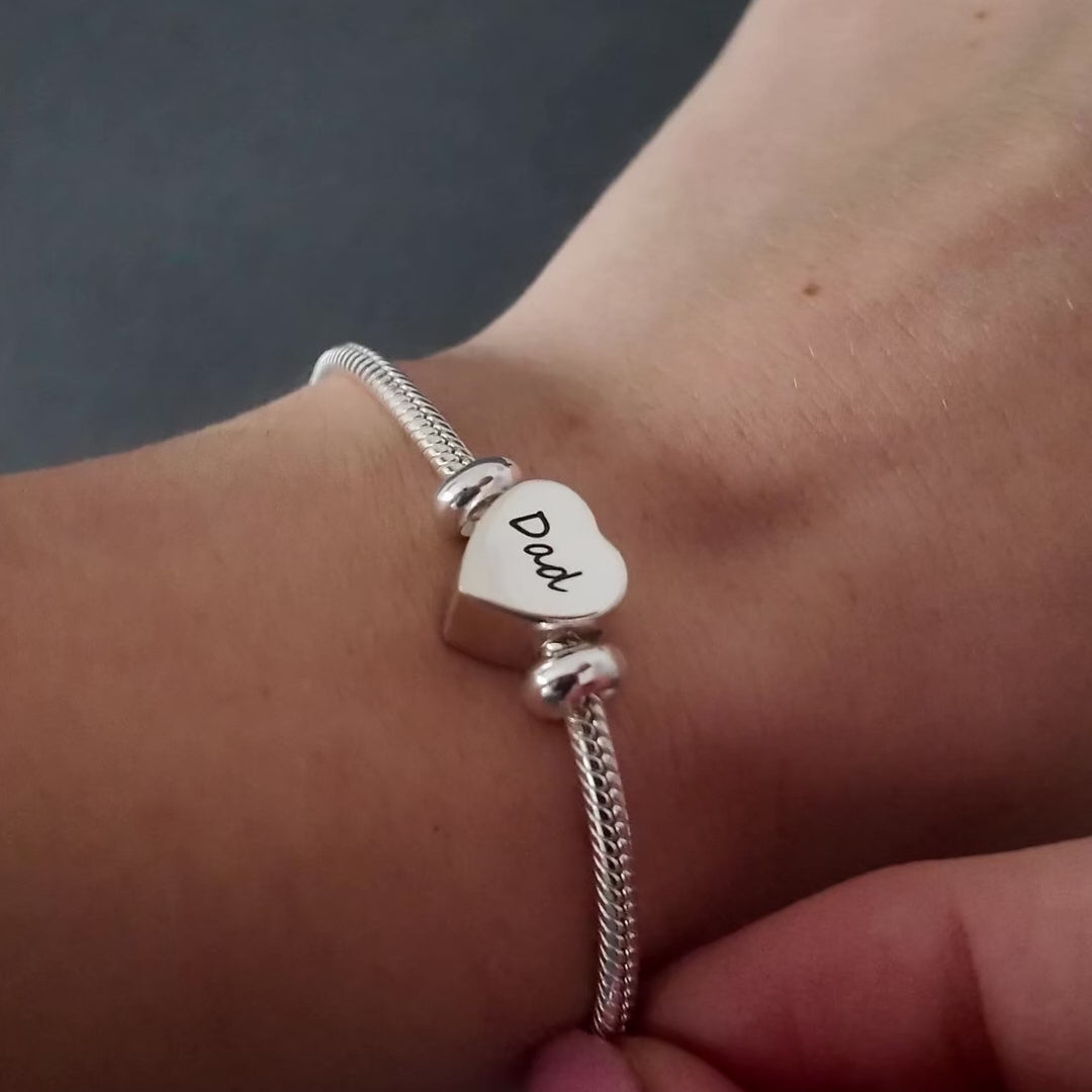 demonstration of a silver heart self fill urn charm. the video shows a womans hands with pink nails unscrewing the urn and using a funnel and stick to fill the urn necklace.