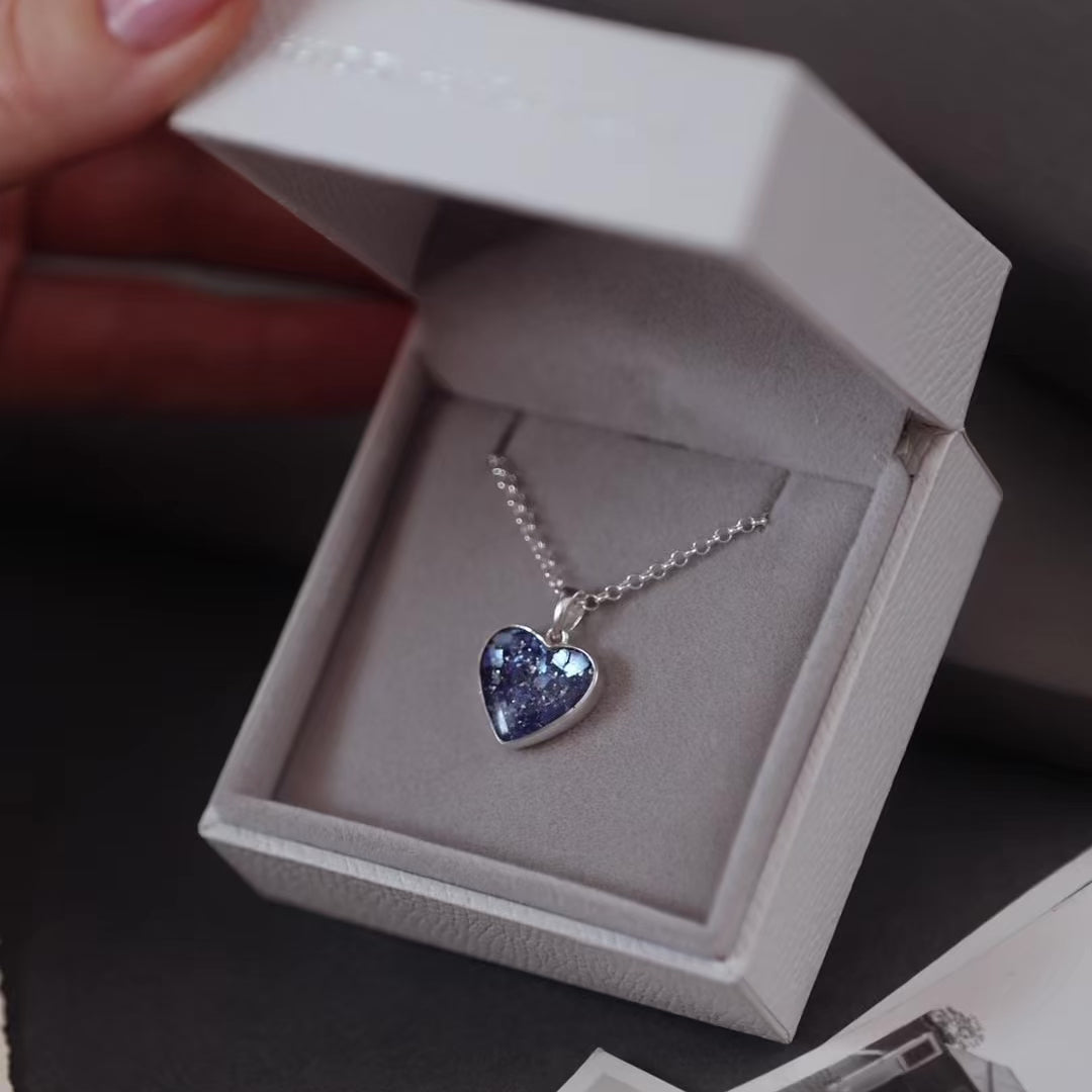 Silver ashes heart pendant necklace with blue crystals in a grey jewellery box held in a women's hand