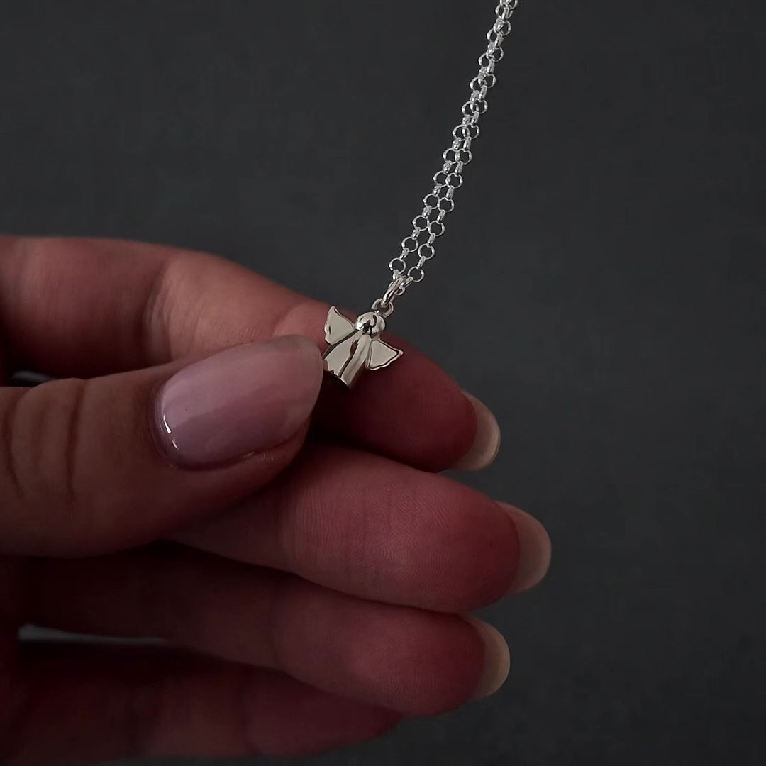 Demo video of womans hands with pink nails showing how to fill a silver small angel urn necklace pendant. it shows her unscrewing the bottom of the pendant with a screwdriver and using a funnel to fill the small angel with cremation ashes. the screw is then screwed back on and the necklace is displayed in a grey jewellery box. 