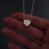 womans hands with pink nails demonstrating how to fill a silver heart pendant agaisnt a dark background. It shows her unscrewing the screw and using a funnel to fill the pendant with ashes. its then displayed in a grey jewellery box at the end.