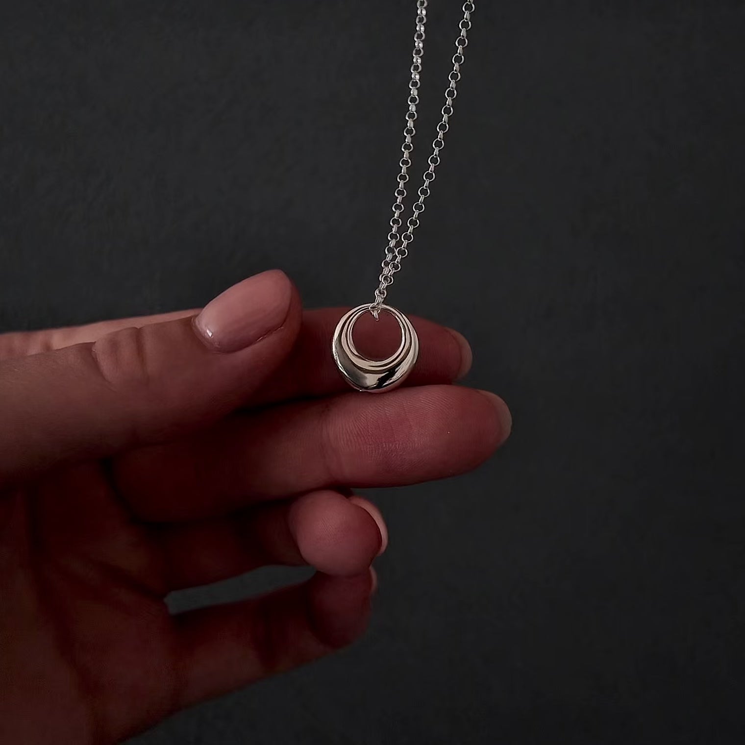 womans with pink nails hands showing a silver circle urn necklace. she is demonstrating how to fill the necklace with cremation ashes by unscrewing the bottom with a screw driver and using a funnel to fill the pendant.