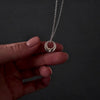 womans with pink nails hands showing a silver circle urn necklace. she is demonstrating how to fill the necklace with cremation ashes by unscrewing the bottom with a screw driver and using a funnel to fill the pendant.