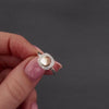 womens hand with pink nails showing a demonstration of filling a silver cluster ring with cremation ashes. she uses a screw driver to remove to screw to the chamber and funnels in the ashes. its then displayed in a grey jewellery box.