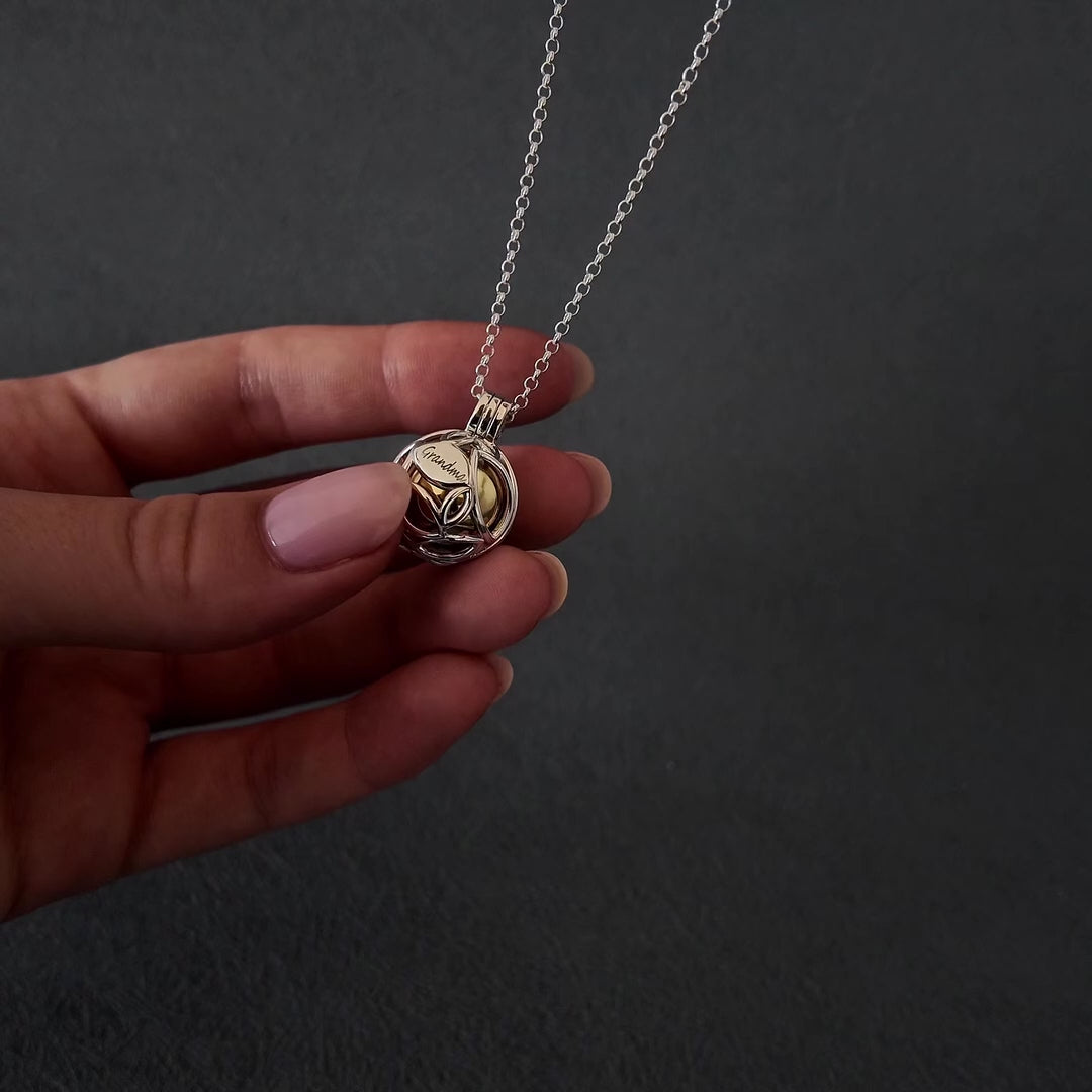 Demo video of womans hands with pink nails showing how to fill a silver leaf cage urn necklace pendant. the pendant has a gold ball inside the cage, to fill with ashes. the video shows her using a wooden stick to fill the ball with cremation ashes.