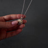 Demo video of womans hands with pink nails showing how to fill a silver leaf cage urn necklace pendant. the pendant has a gold ball inside the cage, to fill with ashes. the video shows her using a wooden stick to fill the ball with cremation ashes.