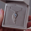 Silver ashes jewellery wing pendant with blue crystals in a grey jewellery box held in a women's hand.