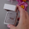 Silver ashes cross over ring with blue crystals in a grey jewellery box held in a women's hand