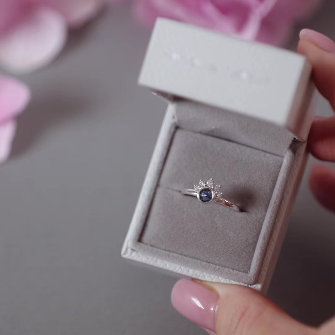 Silver half cluster ashes ring with blue crystals in a grey jewellery box held in a women's hand